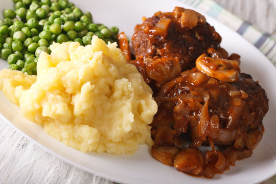 Salisbury steak with mashed potatoes and green peas close-up on a plate. horizontal

