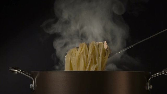 Steaming pasta in a spaghetti spoon on black background