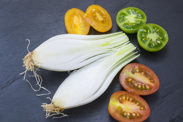 red tomatoes, yellows, greens and spring onions on a board slate
