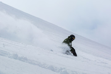 Male snowboarder snowboarding on fresh snow on ski slope on Sunny winter day in the ski resort in...