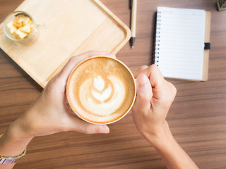 Two hands of woman holding a cup of latte coffee.