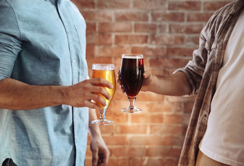 Two men clinking glasses of dark and light beer on brick wall background