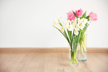 Beautiful fresh tulips and irises on wooden floor against white wall background