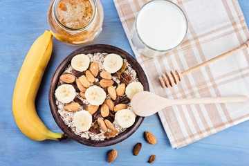 Healthy breakfast. Granola with nuts and  banana in a wooden bowl, honey and  milk  on a blue  background