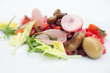 Vinaigrette Russian Salad made of chopped beets, carrots, onion, beans, peas, seasoned with sunflower seed oil, with slices of tomatoes, herbs and sausage, served on a white table