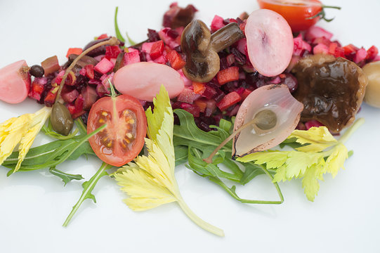 Vinaigrette Russian Salad made of chopped beets, carrots, onion, beans, peas, seasoned with sunflower seed oil, with slices of tomatoes, herbs and sausage, served on a white table