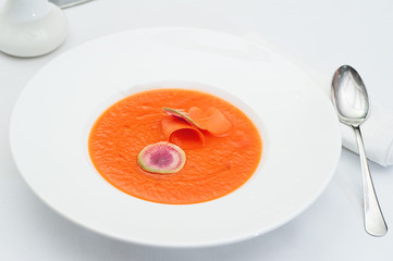 Closeup of Pumpkin Soup with Slices of Water Melon Radish in a White Plate Served on a restaurant table