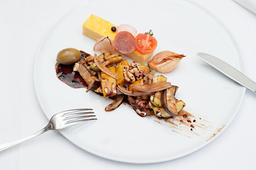 Sliced Polenta Cornmeal with Roasted and Fresh Vegetables Served on a white plate with fork and knife