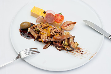 Sliced Polenta Cornmeal with Roasted and Fresh Vegetables Served on a white plate with fork and knife
