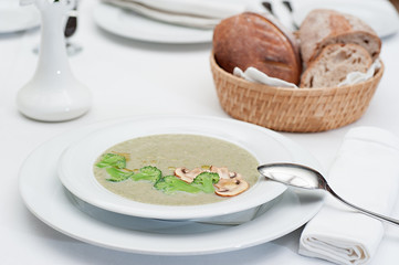 Mushrooms Cream Soup with Broccoli and Mushrooms slices served with freshly baked bread in a basket, on a restaurant table

