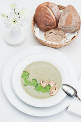 Mushrooms Cream Soup with Broccoli and Mushrooms slices served with freshly baked bread in a basket, on a restaurant table
