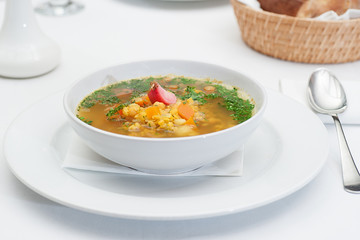 Lentil Soup Served in a White Bowl with Spoon on a restaurant table
