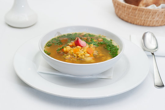 Lentil Soup Served in a White Bowl with Spoon on a restaurant table
