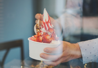 seller pours sauce on a soft frozen yogurt in white take away cup
