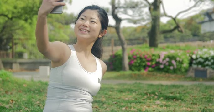 Fun Japanese exercise girl taking selfie with smart phone sitting on grass at the park 