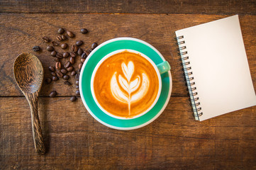 Top view of latte hot coffee, blank note book and wooden spoon in coffee shop. Wooden table background.