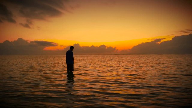 Silhouette of man standing in ocean in prayer during colorful sunrise or sunset