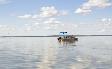Fototapeta na wymiar horizontal image of a pontoon boat coasting on a beautiful blue lake under clear blue sky in the summer time.