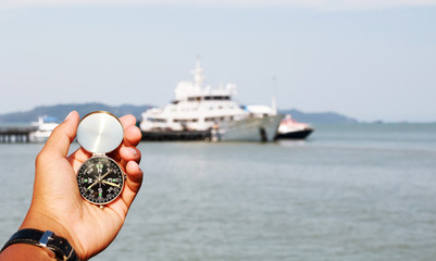 Man hand with a black and silver compass in boat blur background.