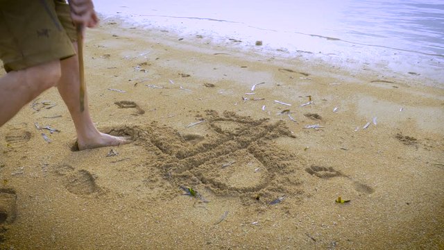 A man runs up to the waters edge and draws a dollar sign in the sand