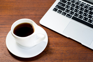 Open laptop and cup of coffee on brown wooden table. 