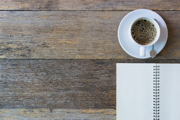Open notebook on wooden background with coffee cup.