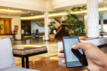 Hand hold and touch screen smart phone, tablet,cellphone on blur image of modern living room at home.