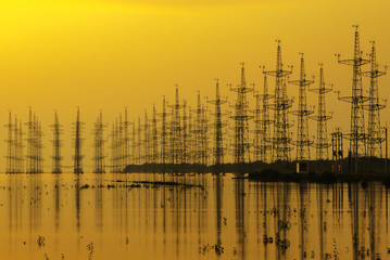 sillouette of Wind turbine at seashore wetland, Impression network at transformer station in sunrise, high voltage up to yellow sky take with yellow tone, horizontal frame 