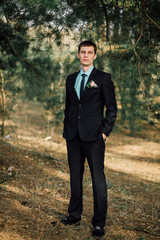 Close up portrait of handsome stylish groom outdoors in park with red bowtie