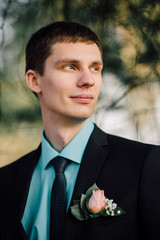 Close up portrait of handsome stylish groom outdoors in park with red bowtie