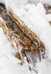 water spring flowing out of wooden channel in snow