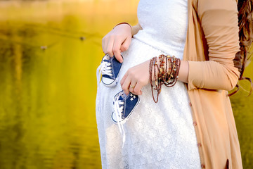 Pregnant woman belly holding baby booties. Healthy pregnancy. Newborn baby booties in parents hands. Pregnant woman belly