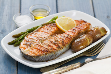 grilled salmon asparagus and potato on white dish on blue wooden background