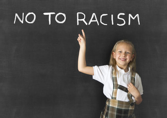 junior schoolgirl with blonde hair pointing with her finger to text no to racism written in classroom blackboard