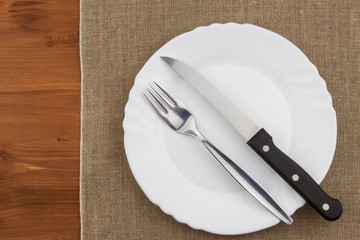 Empty white plate with knife and fork on a wooden table. Waiting for food. Home dining. Directly above view of table setting. Diet food.
