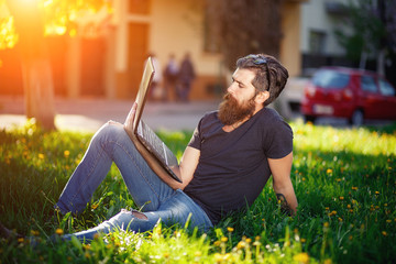 brutal bearded man with a mustache T-shirt, torn jeans and shoes, sitting with a laptop in the...