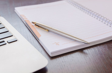 Notepad, pen and laptop on old brown wooden desk. 