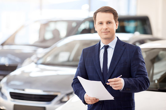 Smiling salesman reading a document at new car showroom