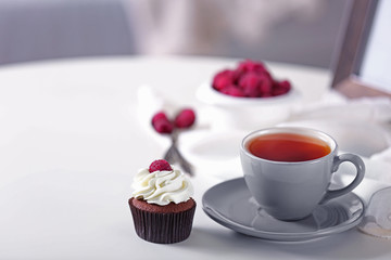 Beautiful chocolate cupcake with raspberry and cup of tea, on table