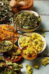 Assortment of dry medicinal herbs in bowls on wooden background top view
