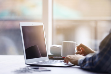 Fototapeta premium Ręce mężczyzny za pomocą laptopa i trzymając filiżankę herbaty przy stole