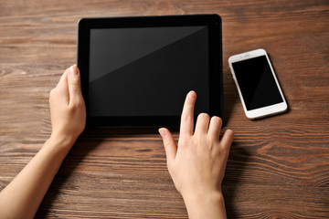 Mobile phone and female hands using tablet, on the wooden background
