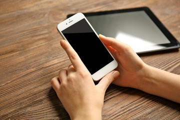 A tablet and female hands using mobile phone, on the wooden background