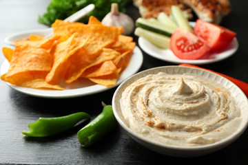 Ceramic bowl of tasty hummus with chips and chili on table