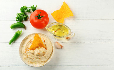 Ceramic bowl of tasty hummus with chips, oil and vegetables on table
