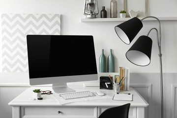 Modern wide screen monitor with lamp on white table in room interior