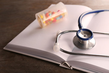 Stethoscope with open book and pills on wooden background. Medical literature concept
