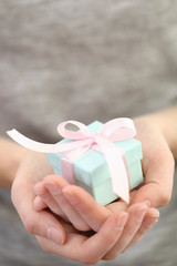 Female hands holding beautiful small gift wrapped with satin ribbon.