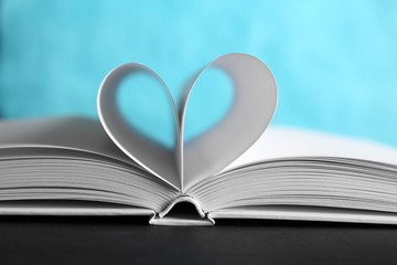 Sheets of book curved into heart shape on unfocused blue background