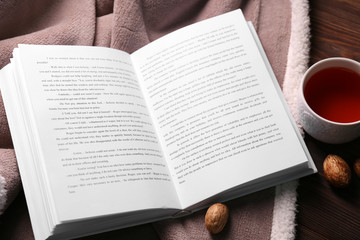An open book, a cup of tea, nuts and a blanket on the floor, close-up